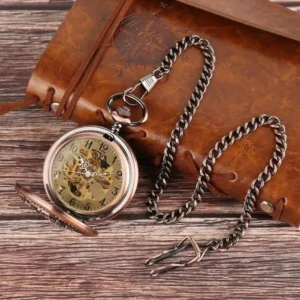 Steampunk mechanical pocket watch with metal chain displayed on leather notebook showing Arabic numeral dial and visible skeleton movement