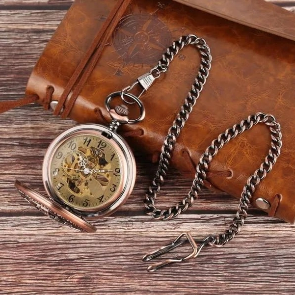 Steampunk mechanical pocket watch with metal chain displayed on leather notebook showing Arabic numeral dial and visible skeleton movement
