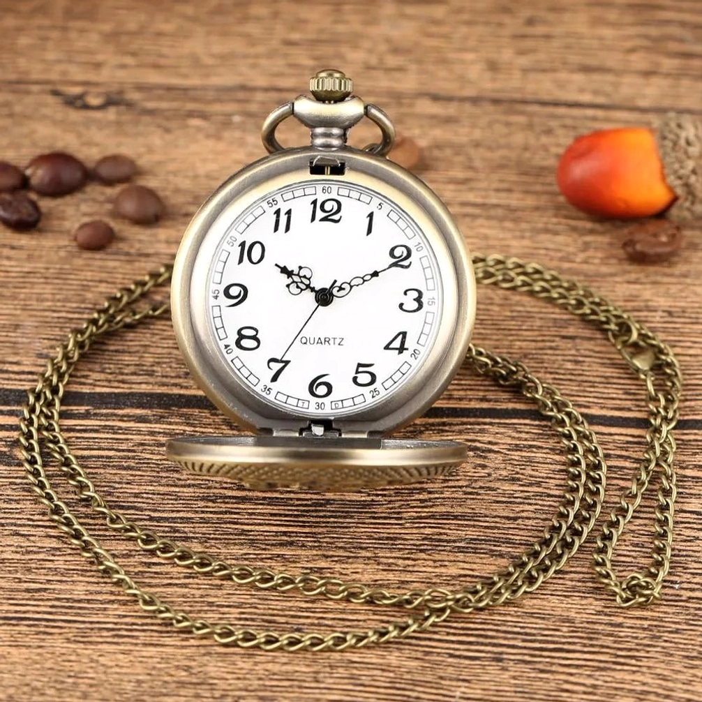 Quartz steampunk pocket watch with white dial, black Arabic numerals, and attached long bronze metal chain on retro wooden desk with vintage coffee props