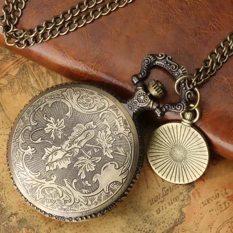 Back of engraved steampunk pocket watch showing floral scroll engravings and radial pattern charm on vintage leather notebook background