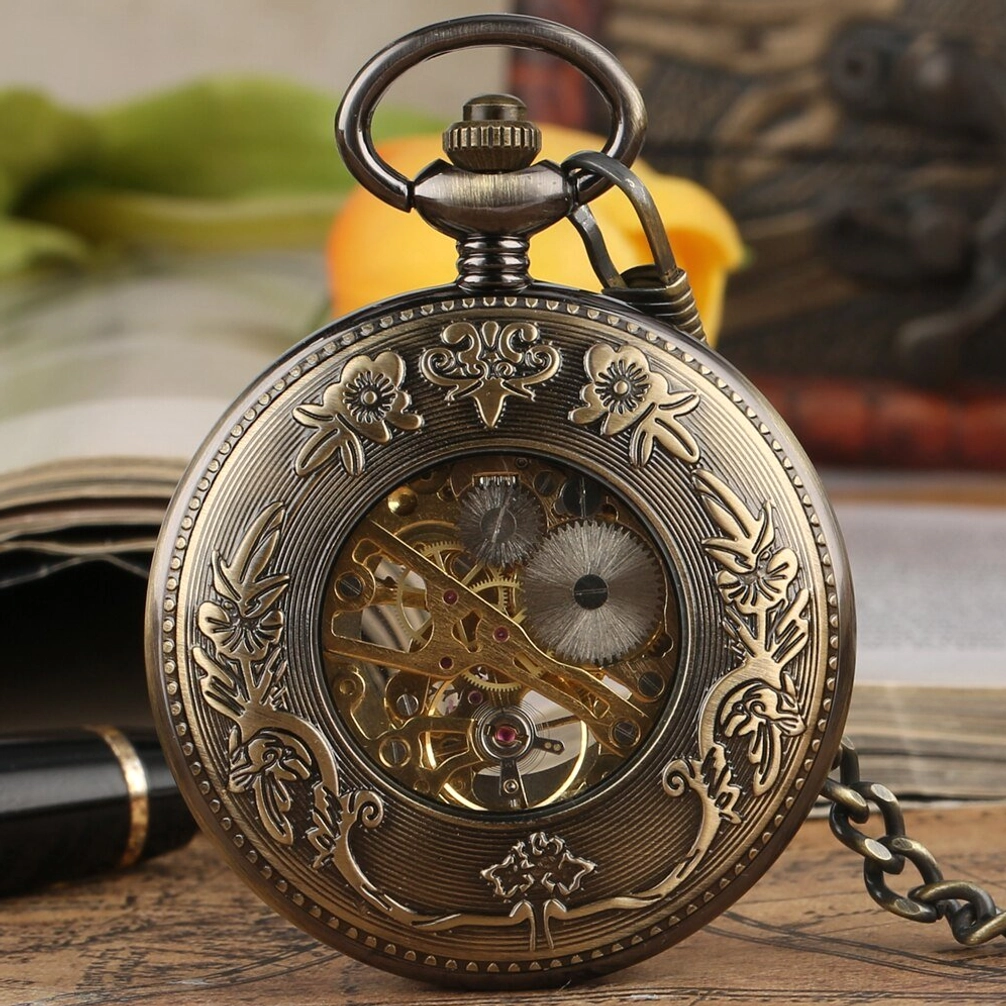 Floral engraved steampunk pocket watch with full botanical carved bronze case and exposed skeleton movement, front close-up on vintage desk with book and flowers