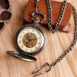 Mechanical steampunk pocket watch flipped open displaying cream dial with red Roman numerals, bronze case with attached metal chain for Victorian-style wear