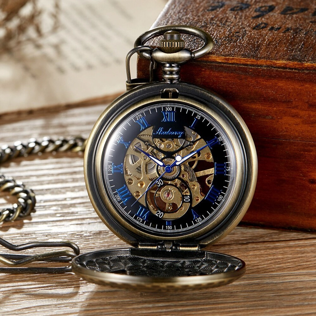 Steampunk mechanical pocket watch with black dial, blue roman numerals, exposed brass gear movement, bronze flip case shown in direct front view on vintage table