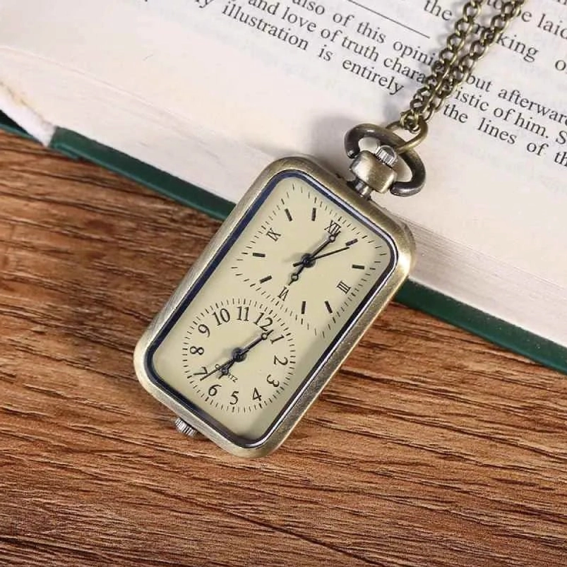 Rectangular steampunk pocket watch with bronze chain shown at oblique angle on wooden desktop next to open vintage book