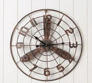 Steampunk propeller wall clock with distressed bronze finish mounted on white shiplap wall, showing full frontal view with cut-out Arabic numerals and industrial radial grid frame