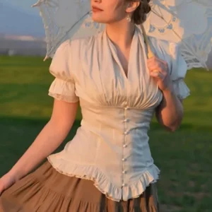 Beige steampunk puff sleeve blouse with vintage Victorian styling, featuring ruched details and ruffled hem, worn by model in outdoor grassland setting