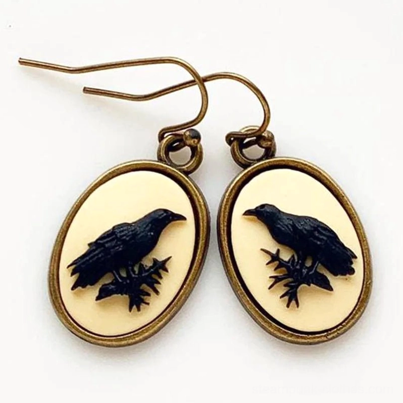 Black raven cameo drop earrings with oxidized bronze frame displayed flat lay on white background, showing straight-on design view and pair detail