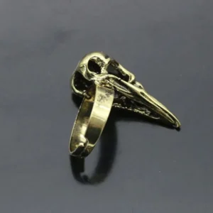 Raven skull steampunk ring side and back view displaying dark patina in carved details, flat metal band, detailed skull shape with weathered vintage aesthetic on dark gray background