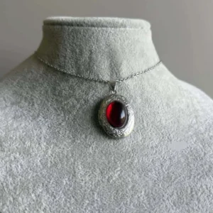 Steampunk red cabochon pendant necklace displayed on jewelry mannequin neck, front view showing ornate engraved silver bezel with deep crimson stone against grey studio background