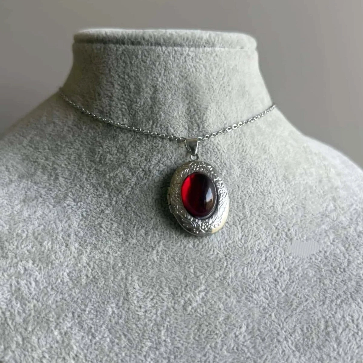 Steampunk red cabochon pendant necklace displayed on jewelry mannequin neck, front view showing ornate engraved silver bezel with deep crimson stone against grey studio background