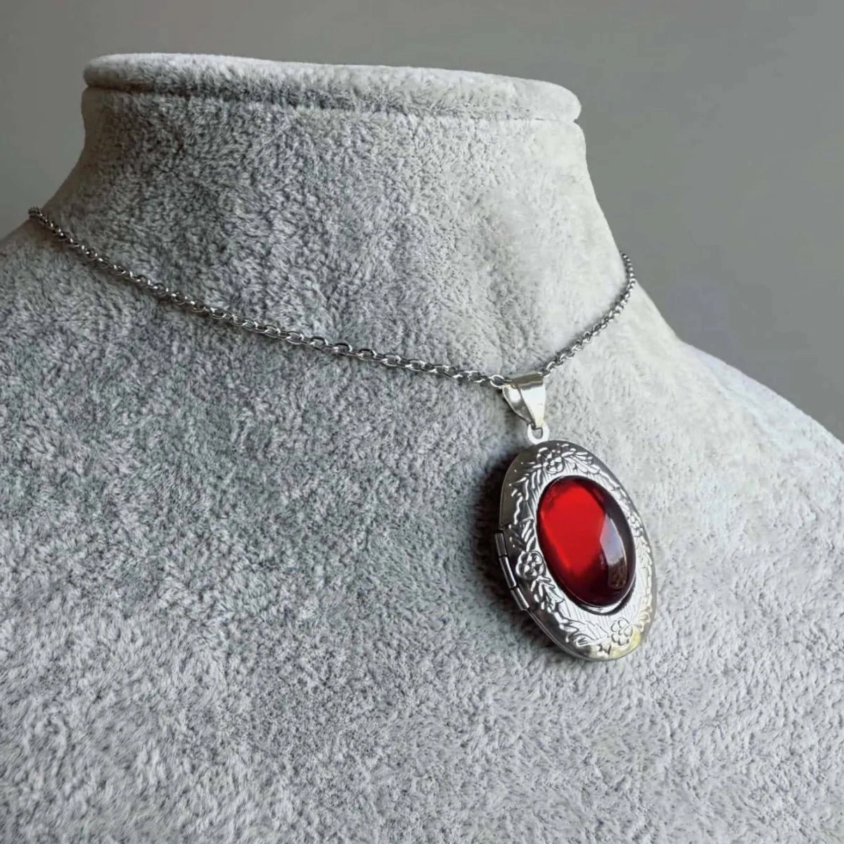 Gothic steampunk red cabochon locket necklace angled close-up on mannequin showing floral engraved silver frame and bright deep red stone detail