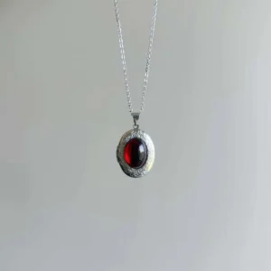 Victorian steampunk red gem pendant hanging overhead view showcasing thin polished silver cable chain and detailed bezel work against light studio background