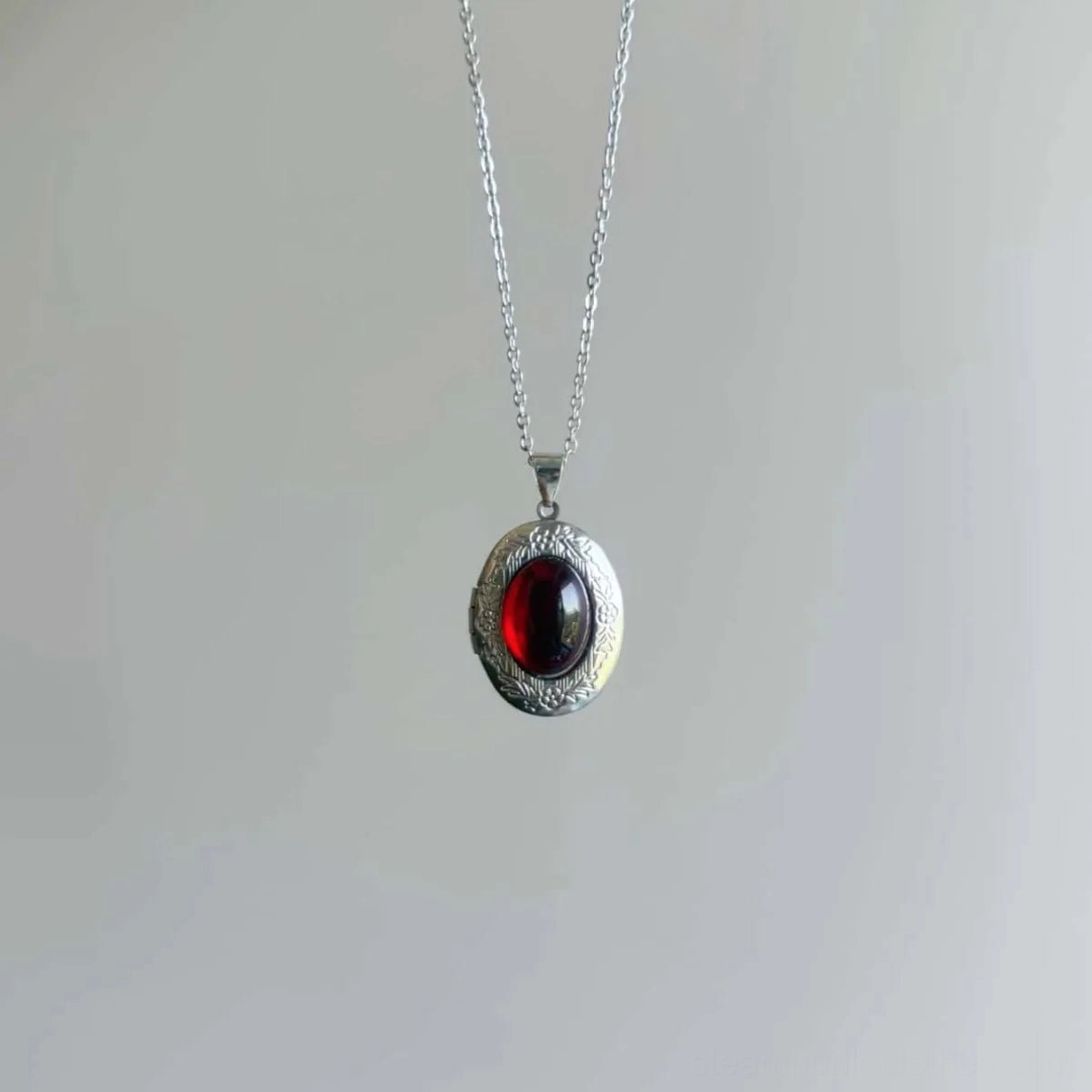 Victorian steampunk red gem pendant hanging overhead view showcasing thin polished silver cable chain and detailed bezel work against light studio background