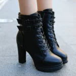 Black steampunk rider lace-up ankle boots with adjustable buckle straps and block heel platform, front close-up view on female model