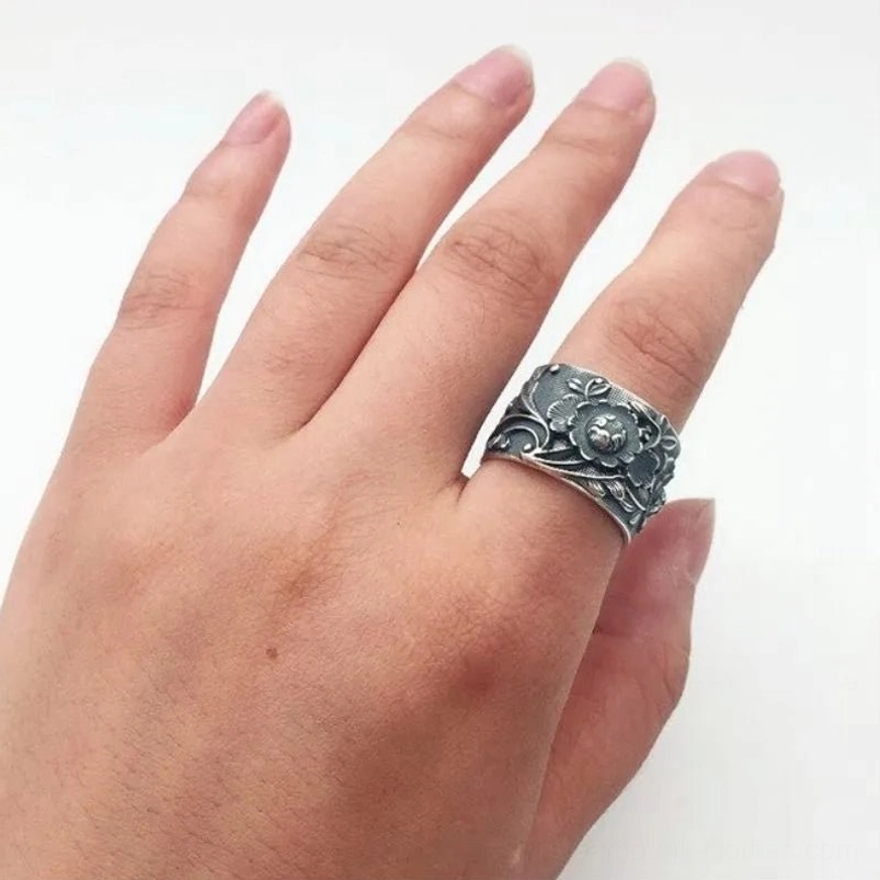 Steampunk floral ring worn on hand showing embossed flower design and adjustable fit, top-down view on white background