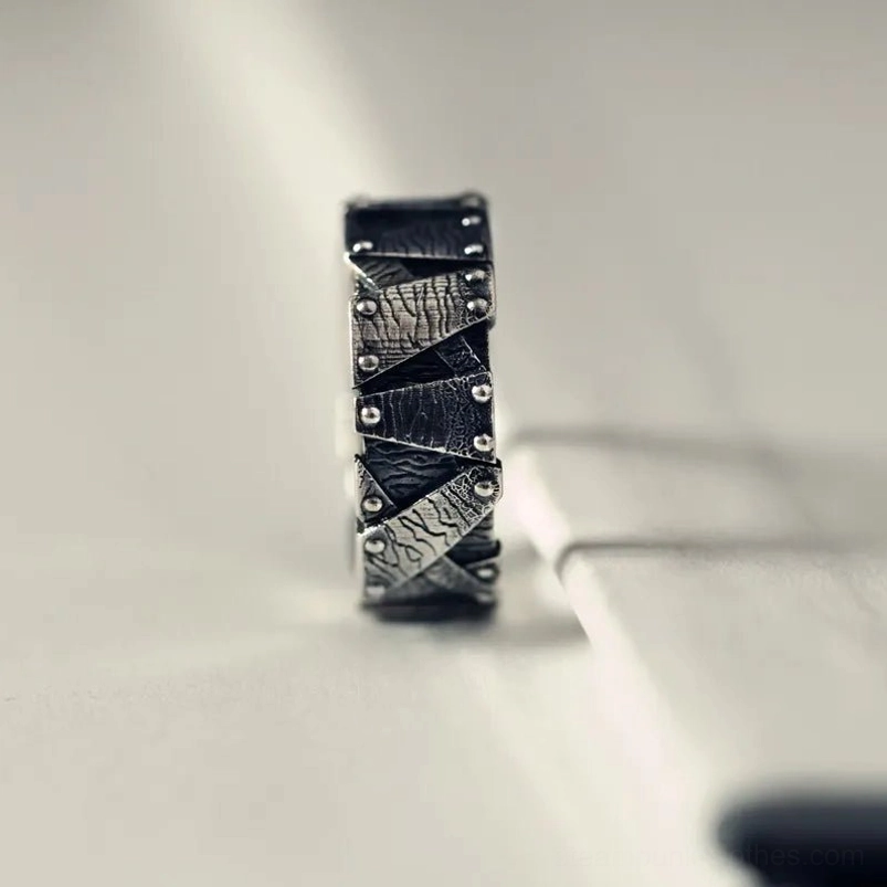 Side profile flat lay of steampunk ring showcasing stacked geometric riveted design in dark silver tone