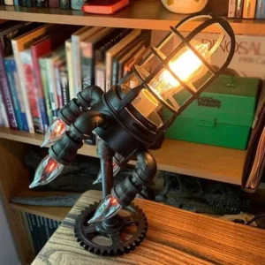 Steampunk rocket desk lamp with aged black metal finish and gear base, displayed on home study desk with bookshelf backdrop, showing three-quarter front view with flame bulbs and industrial design