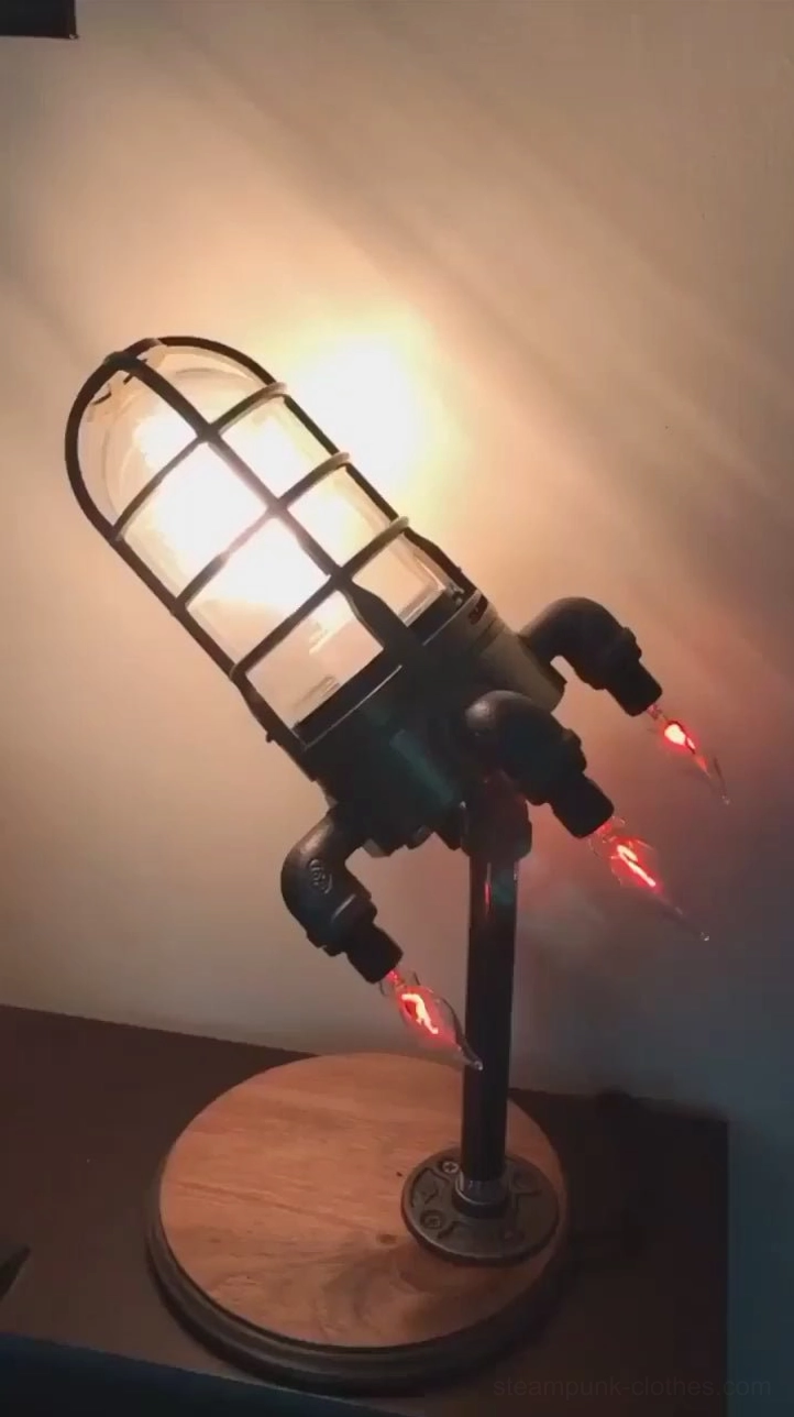 Steampunk rocket desk lamp with black metal finish and wooden round base on small bedside table, front perspective view with warm illumination