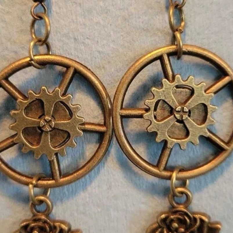 Angled view of steampunk earrings displaying bronze hollow gear wheel mechanism with hanging rose charms