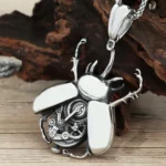 Steampunk scarab beetle pendant necklace with exposed gears and polished wing panels, antiqued silver finish on wooden table with dry wood backdrop
