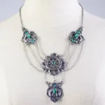 Steampunk layered silver-toned necklace with emerald green crystals and vintage ship wheel engravings, displayed on white mannequin