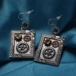 Steampunk silver square gear drop earrings with floral frame design, screw detail and cog decorations on dark teal background