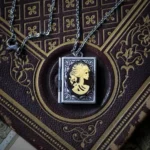 Steampunk skeleton cameo locket necklace featuring intricate black and gold skeleton profile cameo in antique silver-finished frame, displayed on aged vintage leather book with ornate antique styling