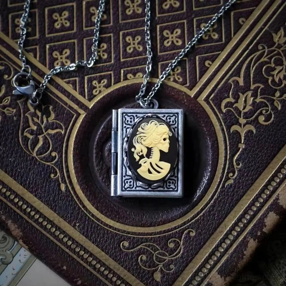 Steampunk skeleton cameo locket necklace featuring intricate black and gold skeleton profile cameo in antique silver-finished frame, displayed on aged vintage leather book with ornate antique styling