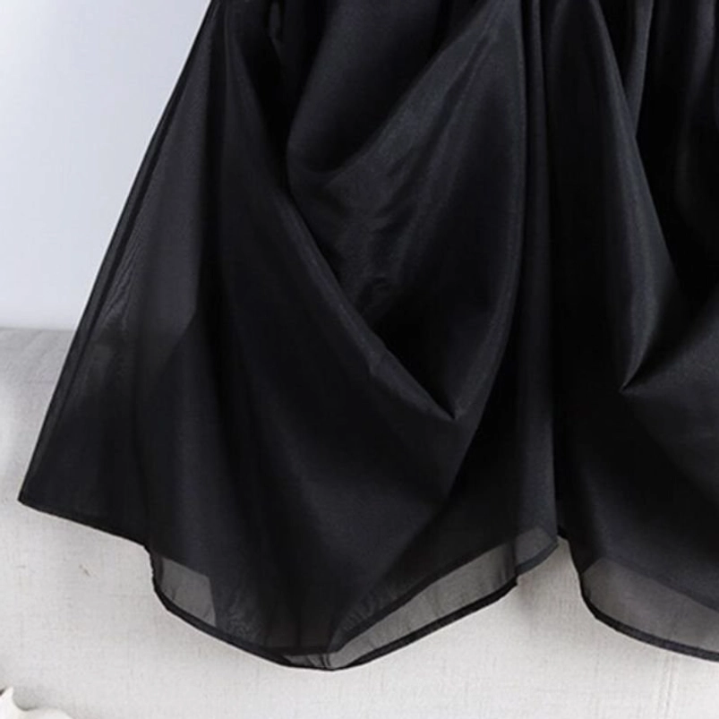 Side view of black steampunk skirt hem showing uneven curved edge, sheer organza mesh drape, and flowy fabric layers creating dynamic silhouette