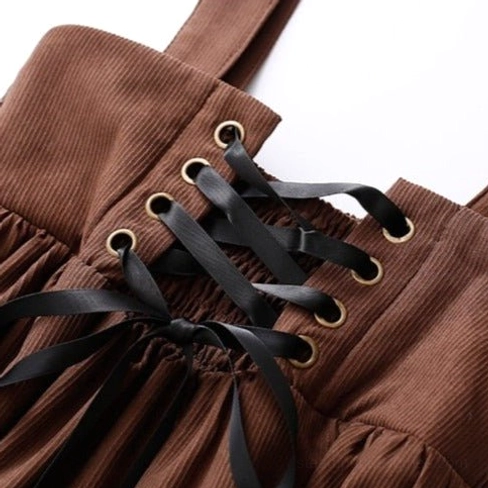 Close-up detail of lace-up waist closure with bronze eyelets, black ribbon lacing, and brown corduroy fabric texture