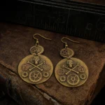 Bronze steampunk skull gear earrings with crossbone design on vintage leather desk with antique ruler, flat lay overhead view showcasing intricate mechanical details