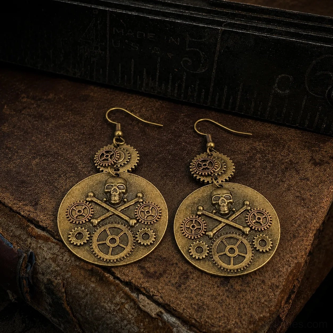 Bronze steampunk skull gear earrings with crossbone design on vintage leather desk with antique ruler, flat lay overhead view showcasing intricate mechanical details