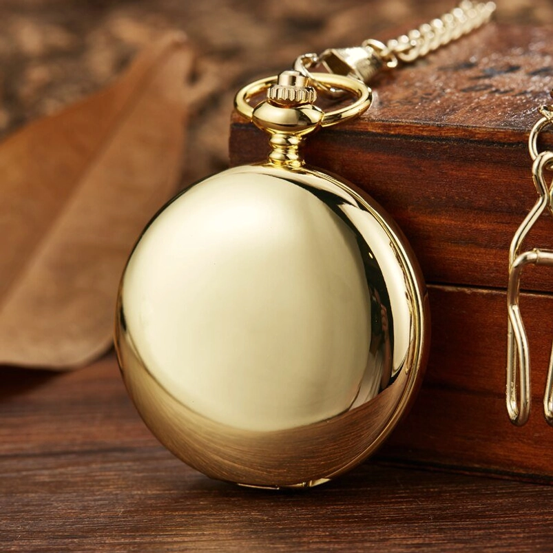 Closed steampunk skull pocket watch three-quarter view showing sealed smooth round case with shiny gold polished metal finish and attached chain, resting on wooden box