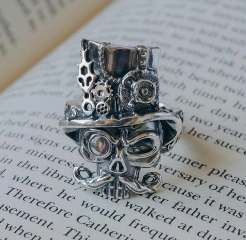 Antique silver steampunk skull ring with top hat mustache and monocle on book page background