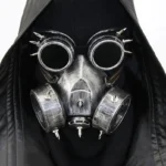 Steampunk spiked gas mask with welding goggles front view on model wearing black hooded leather coat - silver weathered metal finish with dual filter canisters and spike decorations