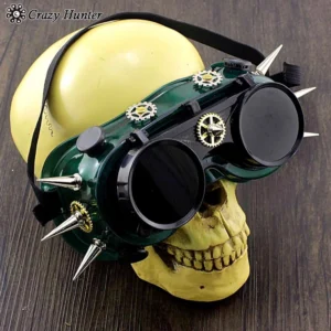Dark green steampunk spiked goggles with silver metal gears displayed on yellow skull mannequin, three-quarter front view showcasing tinted dark lenses and spikes detail on dark wooden surface