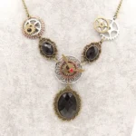 Steampunk vintage statement necklace overhead view featuring mixed metal gears, black faceted faux gemstones, and ornate filigree bezels on textured gray background