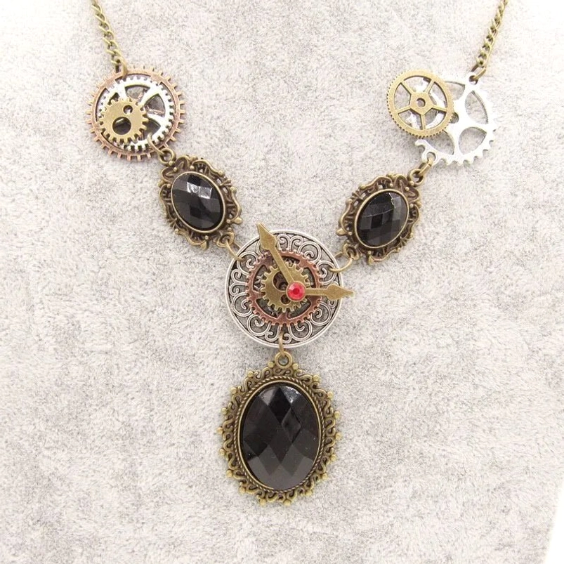 Steampunk vintage statement necklace overhead view featuring mixed metal gears, black faceted faux gemstones, and ornate filigree bezels on textured gray background