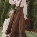 Brown corduroy steampunk suspender skirt front three-quarter view with lace-up waist and ruffled hem, worn outdoors in garden setting