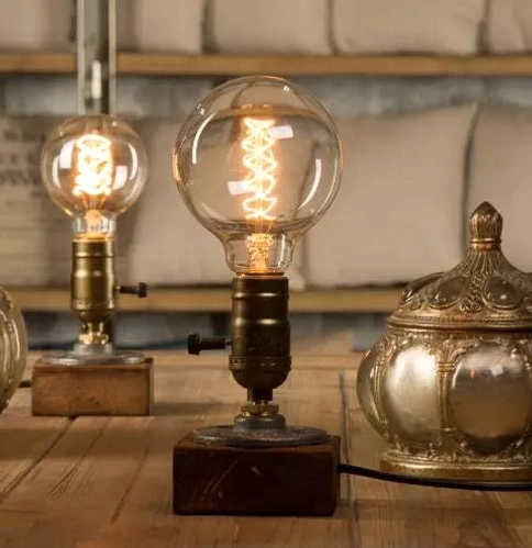 Overhead view of dual vintage Edison bulb steampunk table lamp with round bulbs, aged bronze fixtures, and dark wood base on wooden table