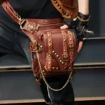 Steampunk leather thigh holster bag with brass rivets and studded details worn on male model, close-up side view showcasing industrial brown leather construction and vintage hardware