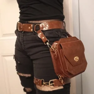 Steampunk leather thigh bag worn on hip with dark brown faux leather and gold twist-lock closure, styled with black ripped shorts for edgy rebellious aesthetic effect