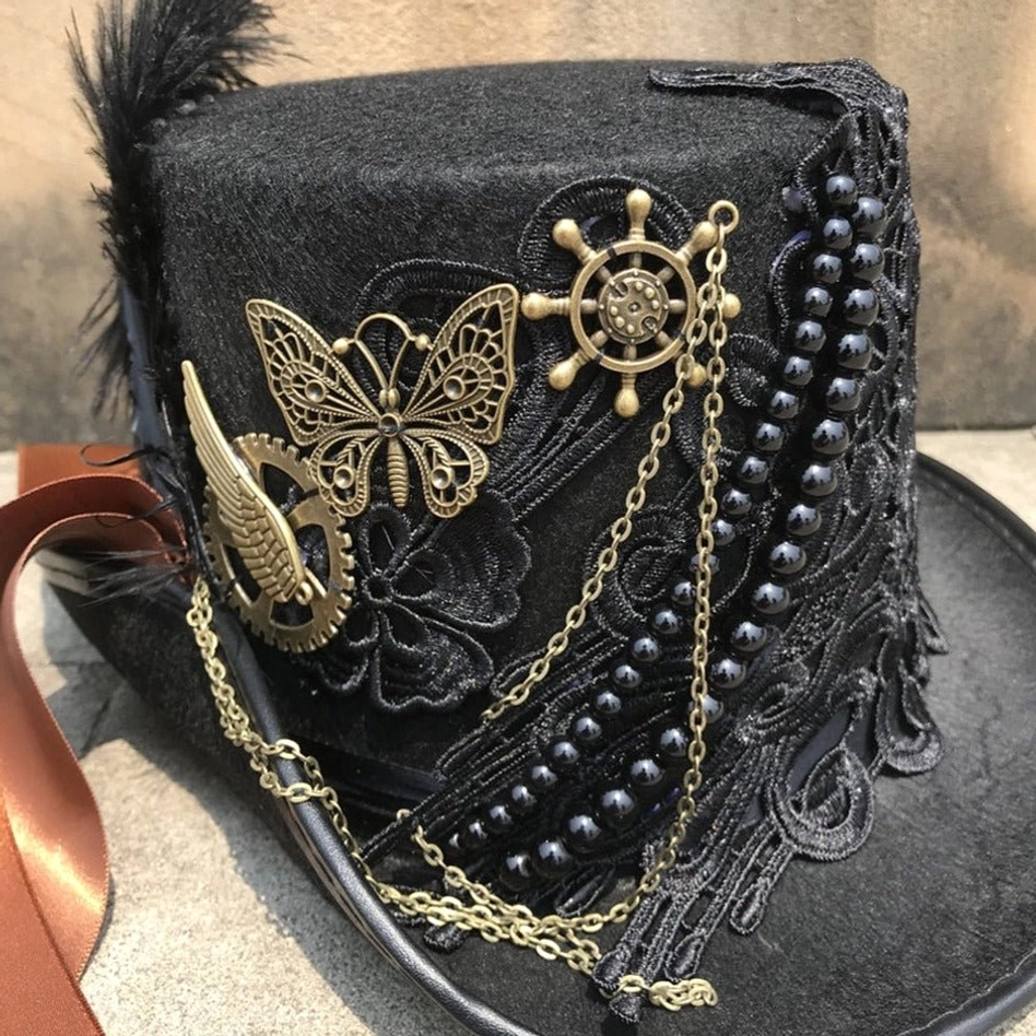 Steampunk top hat close-up front view showcasing intricate black lace, layered gold chains, black bead strands and bronze hardware ornaments on stone pavement