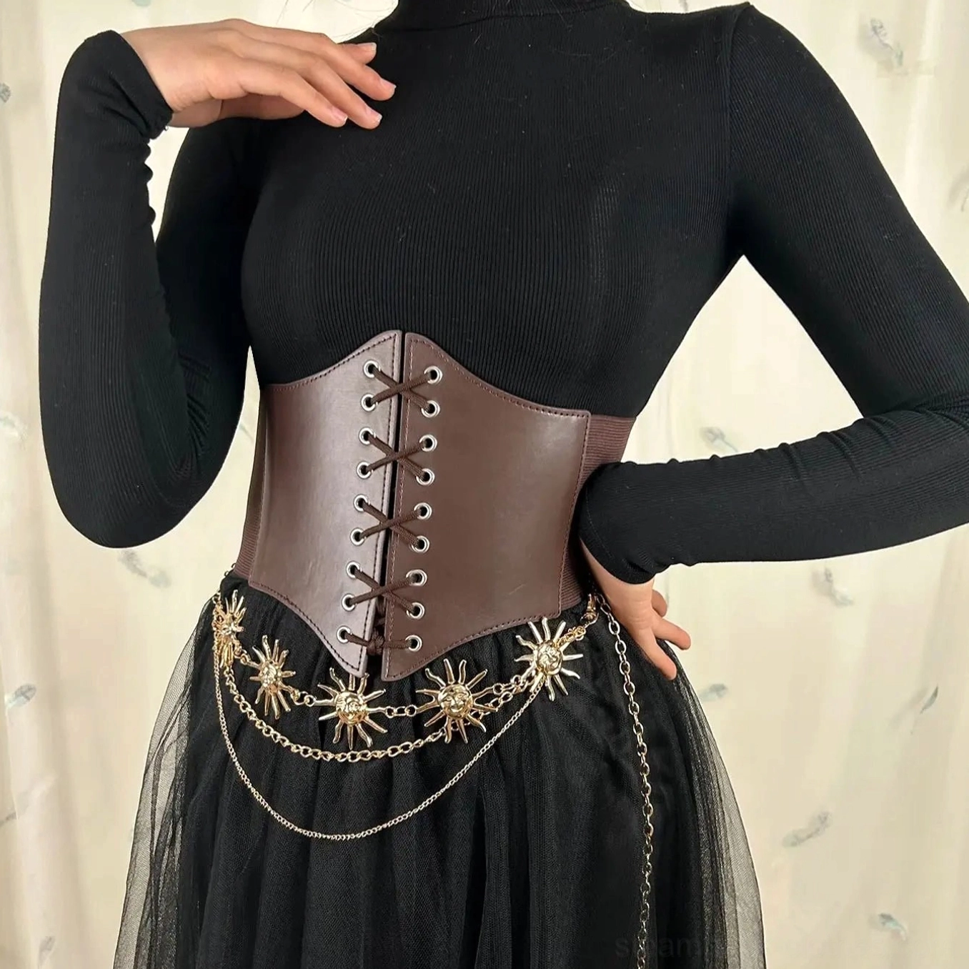 Underbust corset belt with ornate layered gold sun chains styled with black turtleneck top and gothic tulle skirt, three-quarter front view emphasizing dark elegant steampunk aesthetic