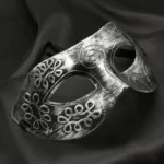 Distressed silver steampunk Venetian masquerade mask with embossed scroll and floral motifs, shown from oblique side angle on dark backdrop