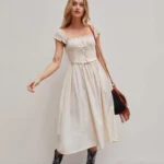Beige steampunk Victorian corset dress with smocked bodice, square ruffled neckline, and A-line ankle-length skirt worn by blonde model in studio setting