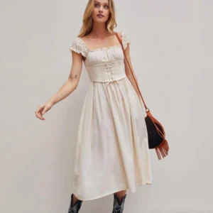 Beige steampunk Victorian corset dress with smocked bodice, square ruffled neckline, and A-line ankle-length skirt worn by blonde model in studio setting