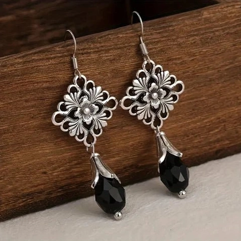 Steampunk Victorian silver filigree flower drop earrings with black faceted crystal teardrops, side view on wooden background