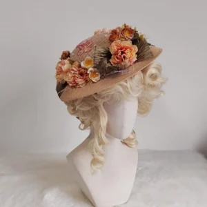 Steampunk Victorian wide-brimmed floral hat with woven straw texture and pleated brown trim, displayed on mannequin with blonde curly wig, left side view on white plush tabletop