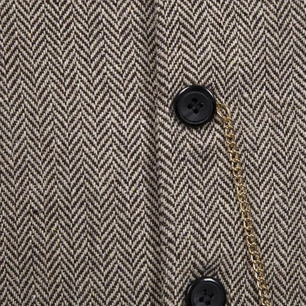 Close-up macro detail of steampunk waistcoat showing herringbone woven texture fabric, black round buttons and gold decorative chain embellishment